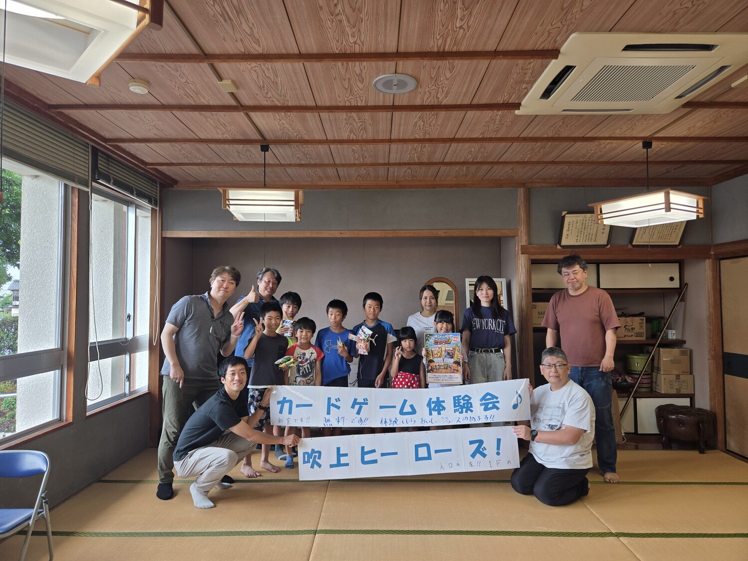カードゲーム体験会の集合写真(横断幕を囲む参加者のみなさん)